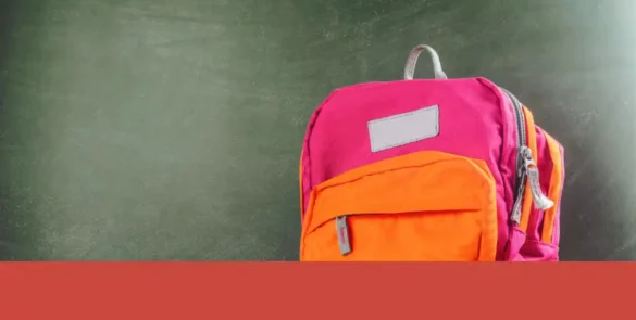 Mochila escolar en tonos rosa y naranja situada frente a un pizarrón verde texturizado, representando el entorno educativo y los productos de licencias escolares para niños.