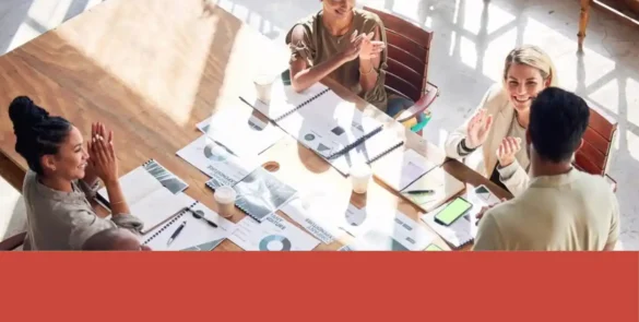 Equipo de marketing de una pyme reunido alrededor de una mesa revisando gráficos, documentos y dispositivos durante la planeación de una campaña de temporada y su presupuesto.