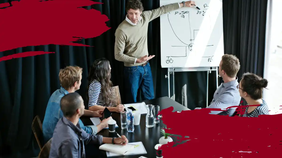 Group of professionals in a meeting, listening to a leader presenting strategies on a whiteboard, emphasizing leadership and strategy planning.