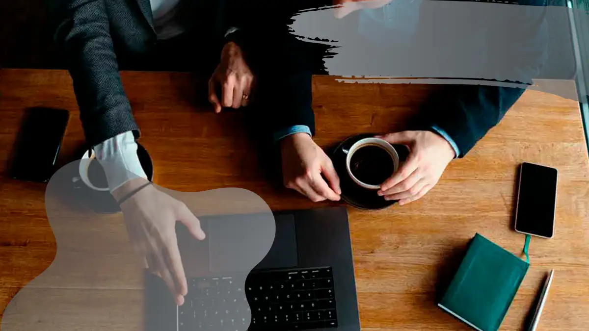 Two professionals collaborating over a laptop, with a coffee cup on a wooden table, discussing strategies.