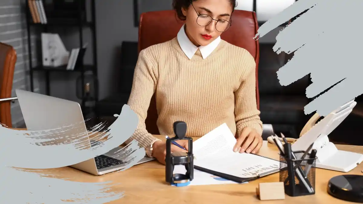 Professional woman working at her desk, reviewing documents with a laptop and office supplies nearby.