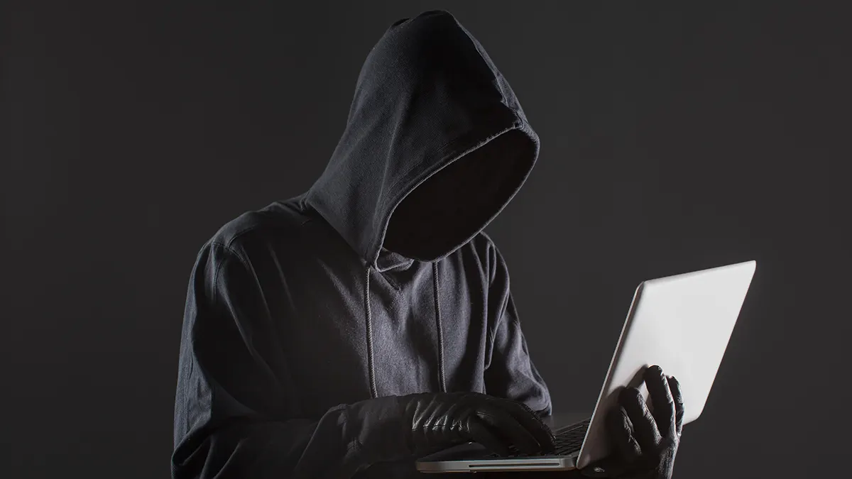 Persona encapuchada usando una laptop en la oscuridad, representando amenazas de fraude digital en México