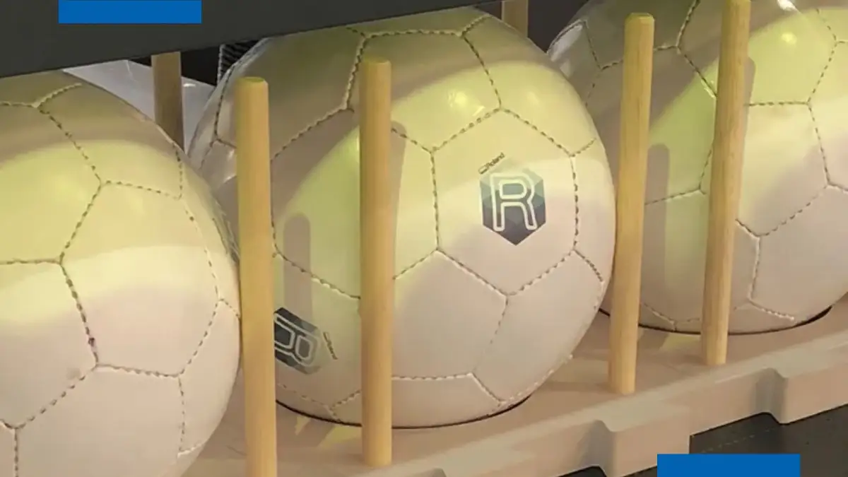 Personalización de balones con impresión UV de Roland. Balones de fútbol personalizados con impresión UV mostrando el logotipo de Roland, alineados en una estructura de exhibición, destacando la aplicación de tecnología de impresión en objetos deportivos.